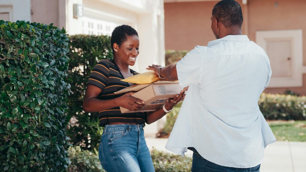 A smiling woman receives multiple packages from a delivery man outdoors.